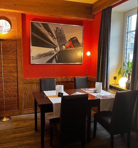 Restaurant London Gemütlicher Restaurantbereich mit Tisch, Stühlen und schwarzem Wandbild.